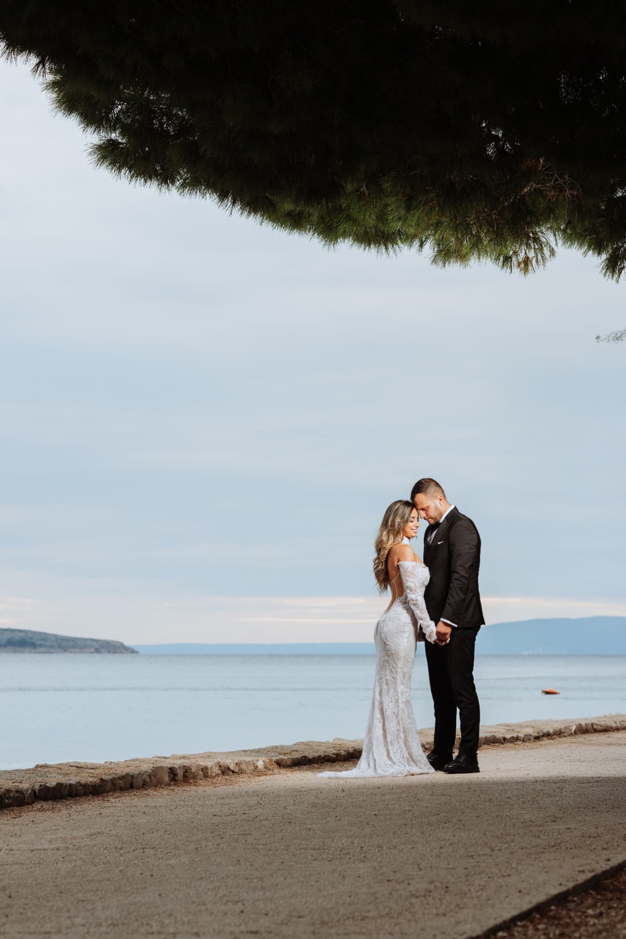 Ana and Stefan during their wedding couple session on Cres Island, Croatia, standing by the sea beneath a pine tree.