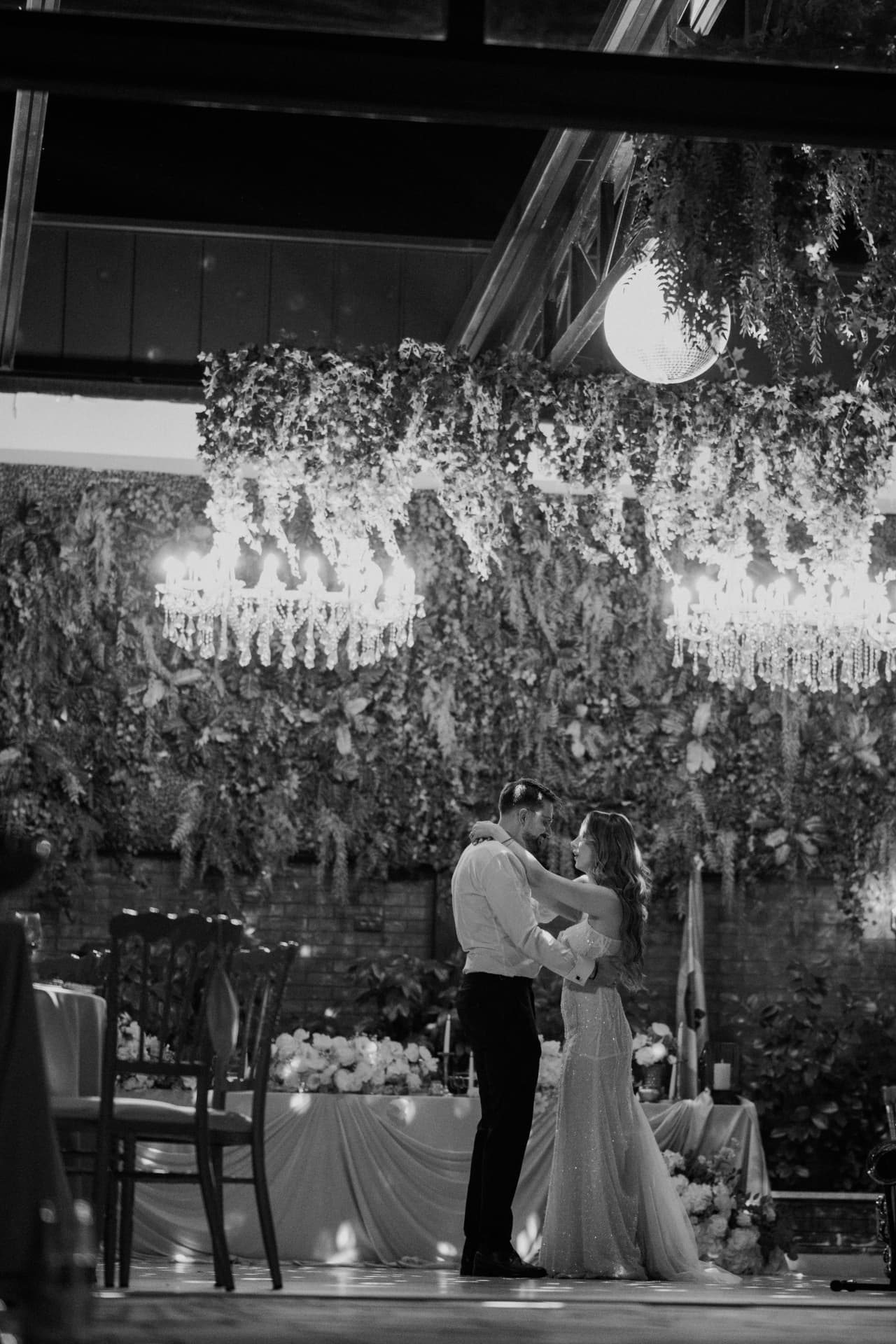 Black-and-white photograph of the couple dancing beneath chandeliers and a hanging greenery installation at Verde Open Concept, Belgrade