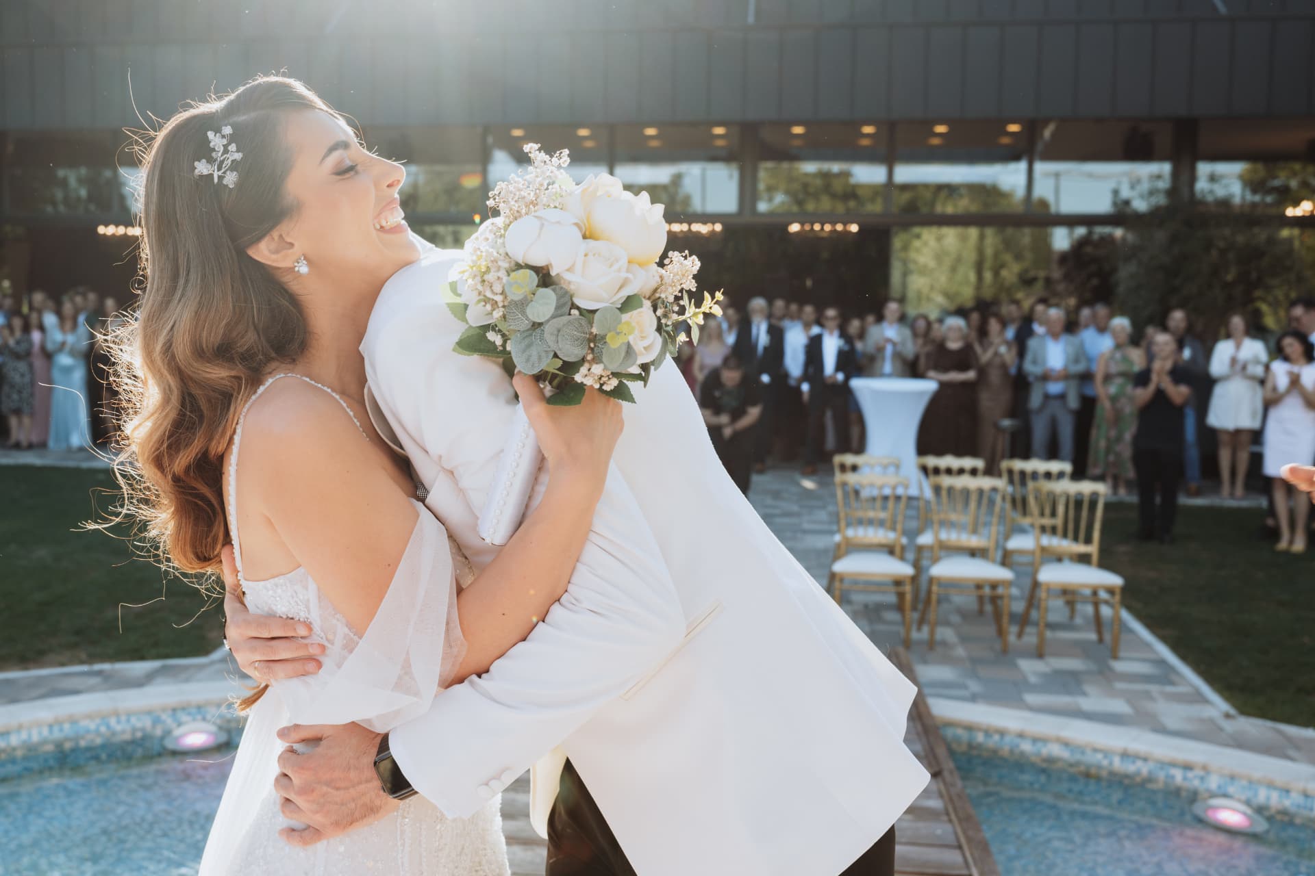 Bride laughing as she embraces the groom after the outdoor ceremony, with guests applauding behind them
